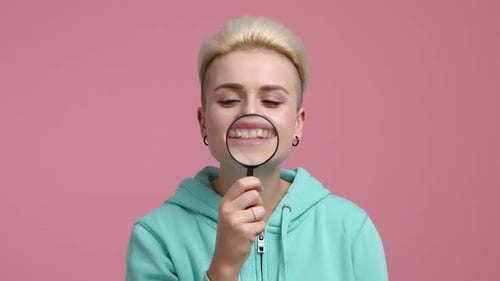 Woman Smiles Through Magnifying Glass on Pink Background