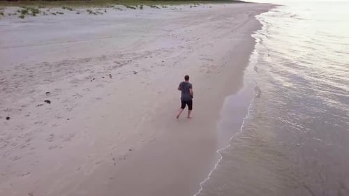 Aerial Shot of Man Running On Sandy Beach on a Cloudy Day. Beach Run Slowmotion. Man Jogging on a Be
