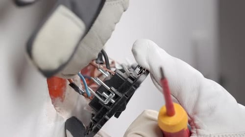Gloved Hands Repairing Electrical Outlet with Screwdriver