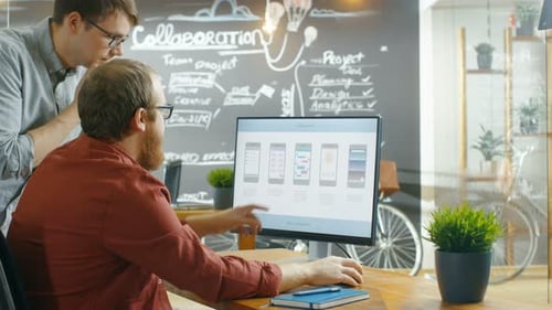 Two Male Mobile Game Application Developers Talk while Working on a Personal Computer, Designing Wi