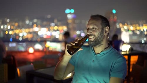 Man enjoys a refreshing cocktail at a luxurious rooftop bar at night