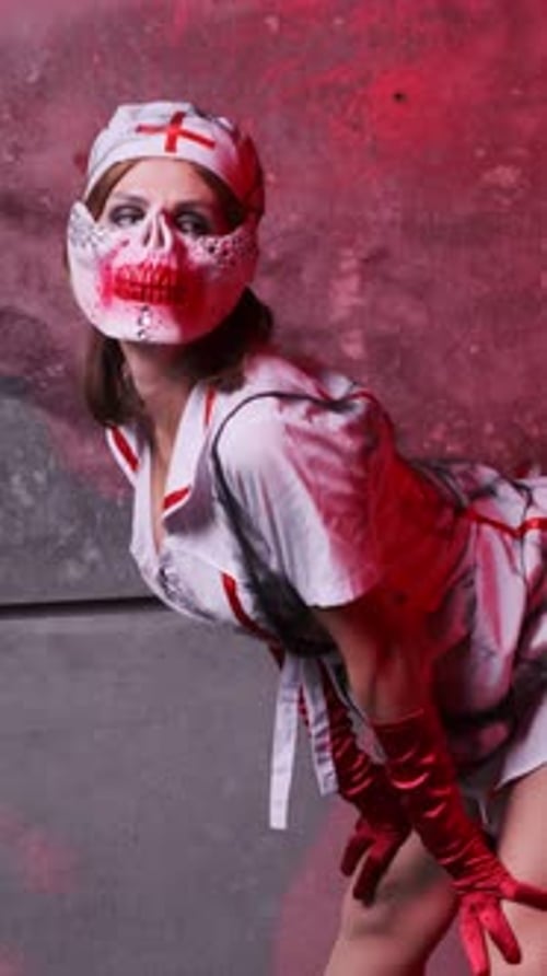 Beautiful sexy girl in scary nurse costume, red gloves and scary mask for Halloween. Posing leaning