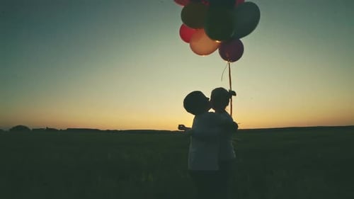 Children Hold Balloons and Embrace in Field at Sunset