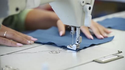 Close up view of dressmaker woman that makes clothes on sewing machine in factory
