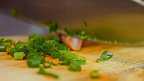 a Woman's Hand Cuts Green Onions with a Knife on a Wooden Chopping Board