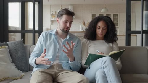Couple sur un canapé, un homme explique tandis qu'une femme écrit des notes dans un carnet