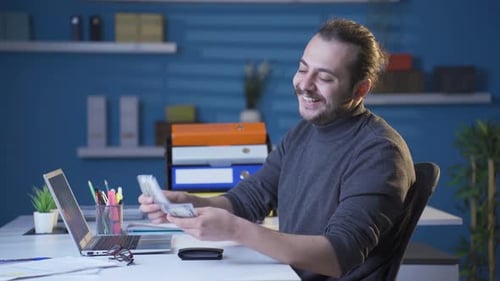 Smiling Young Adult Man Counting Money at Desk