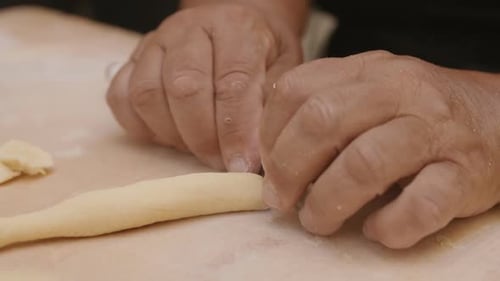 Close up slow motion footage of old weathered hands cutting a roll of dough to make pasta shells.