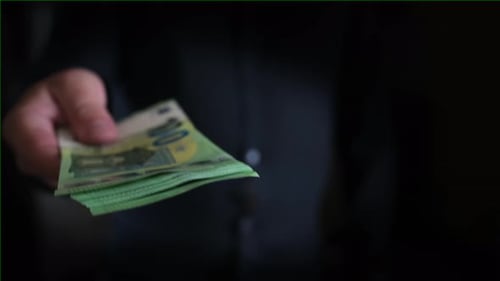 Man's hand holds out stack of one hundred euros bills to another person, close-up