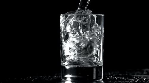 Clear Liquid Being Poured Over Ice in Glass