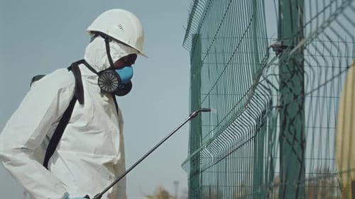 Ecologist in Coverall and Respiratory Mask Using Backpack Sprayer