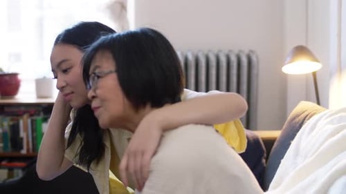 Teen Girl Embraces Senior Woman on Couch Indoors