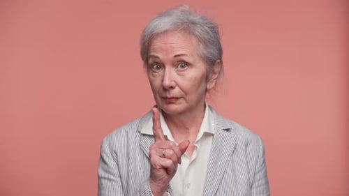 Ernsthafte Seniorin gibt Warngeste auf rosafarbenem Hintergrund