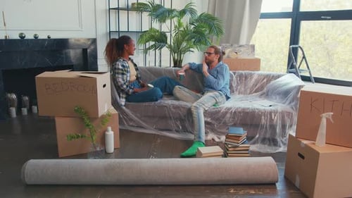 Young Happy Diverse Couple From Woman and Man Prepared to Move Sits at Sofa