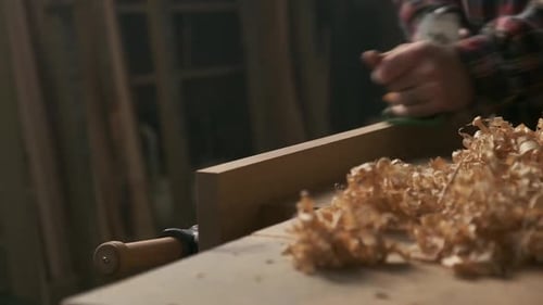 Carpenter planing wood in moody workshop