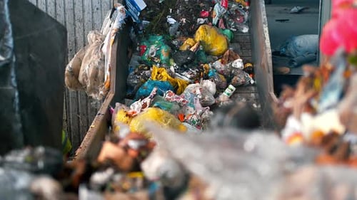 Workers loading garbage onto a conveyor belt at waste sorting plant. Slow motion