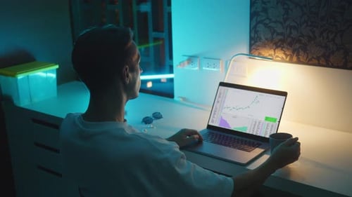 Trader Works Late at Night Analyzing Stock Market Charts on Laptop Trading Success and Profit Growth