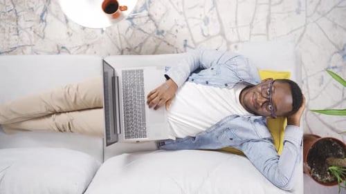 Man Works on Laptop While Relaxing on Couch