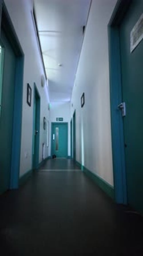Low angle POV shows an empty hospital corridor with teal doors and a dark floor The central.