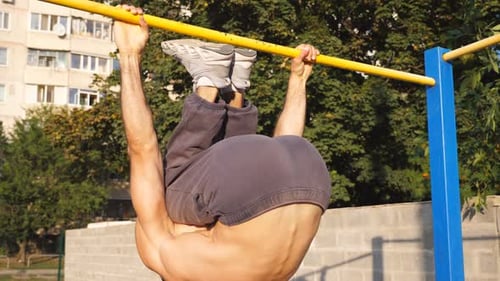 Close Up to Young Muscular Athlete Showing Some Gymnastics Stunts on Horizontal Bar Outdoor