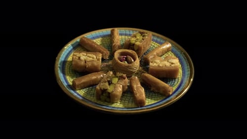 Gold-rimmed plate of baklava pastry dessert rotates on black background