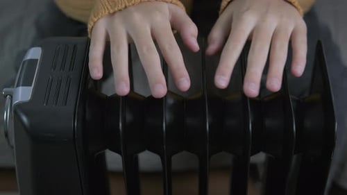 Hands of a Teenager Girl on an Electric Radiator