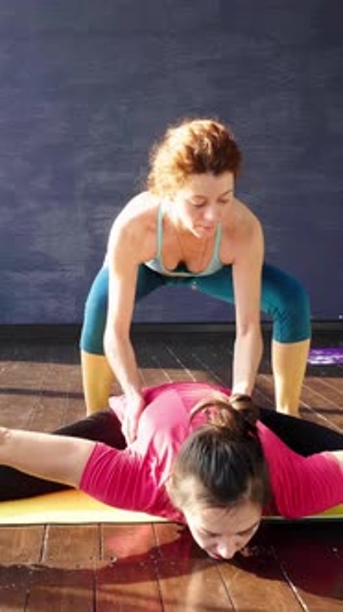 Yoga Instructor Assisting Student in Stretching Exercise on Mat in Bright Studio Environment