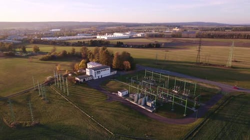 Flight over electricity substation and high voltage pylons on the outskirts of the city at sunset in