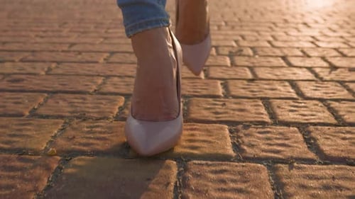 Slim Female Legs in HighHeeled Shoes Walk in the Sunset Light in City Park