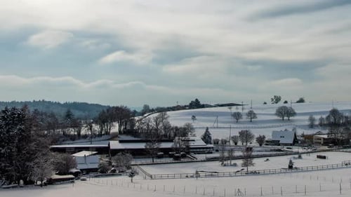 Cloudy Weather in a Hilly Area with a Winter Village with Snowcovered Farms