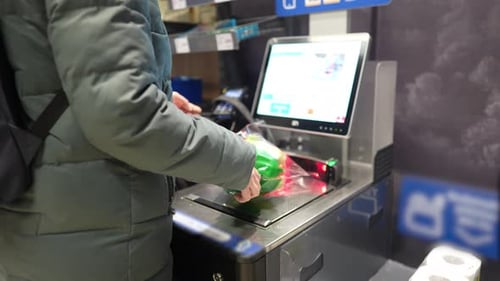 the girl scans the goods at the self-service checkout and pays for the purchase using the phone