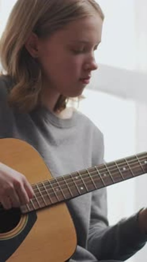 Teen Girl Plays Acoustic Guitar Indoors by a Window