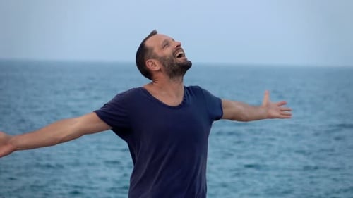 Young man dancing turns around happily near the sea in super slow motion