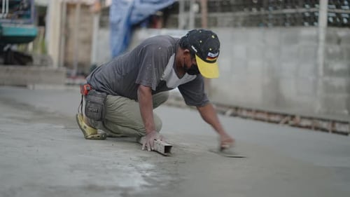 Road Construction Worker In Mask Using Finishing Trowel To Smooth Freshly Poured Concrete On The