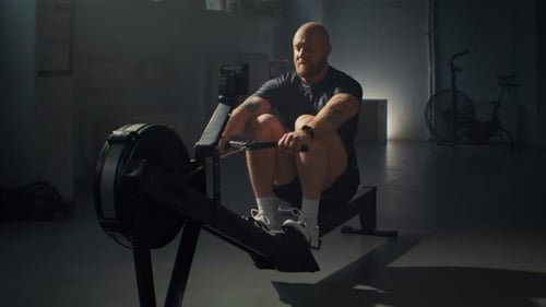 Baldhead Man in Activewear Exercises on Rowing Machine in Gym