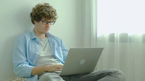 Young Adult Works on Laptop by Window