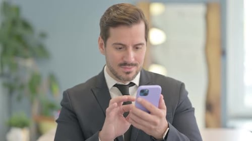 Man Celebrates Success on Smartphone in Workplace