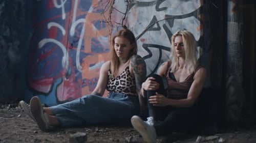 Two Young Women Sit Against Graffiti Wall