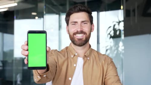 Handsome businessman presenting mobile phone with green screen standing in modern business office.