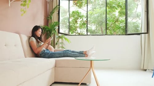 Woman Relaxing on Sofa with Smartphone Indoors