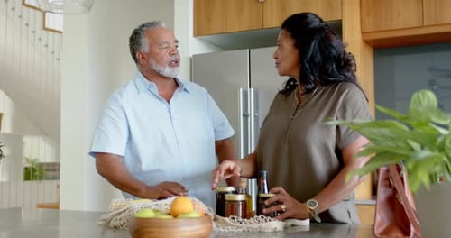 Pareja afroamericana desempaca una bolsa de malla reutilizable, coloca los frascos en la isla de la cocina y almacena la comida