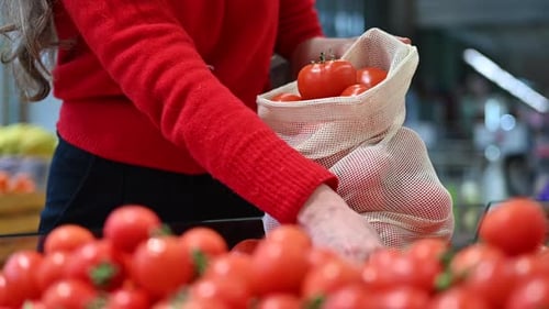 Mujer recogiendo tomates en una bolsa reutilizable en una tienda. Temáticas del Día de la Tierra y la Ecología. Cámara lenta