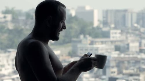 Man drinking coffee, using phone in apartment