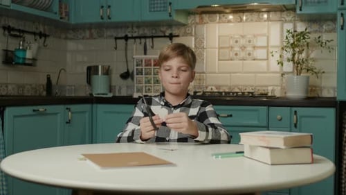 Blond-Haired Boy Cutting White Paper at Kitchen Table