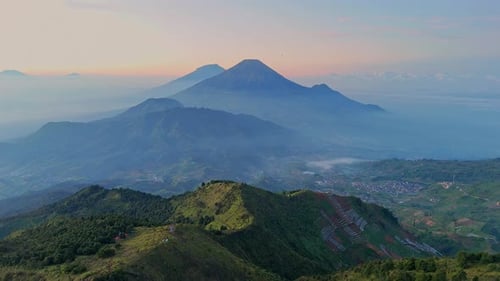 Drone shot of greenery mountain range landscape with layered hills, farmland, and distant mountains