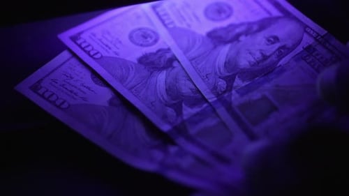 One Hundred Dollar Bills Under Blue Light