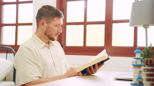 Man Reading Book Indoors by Window