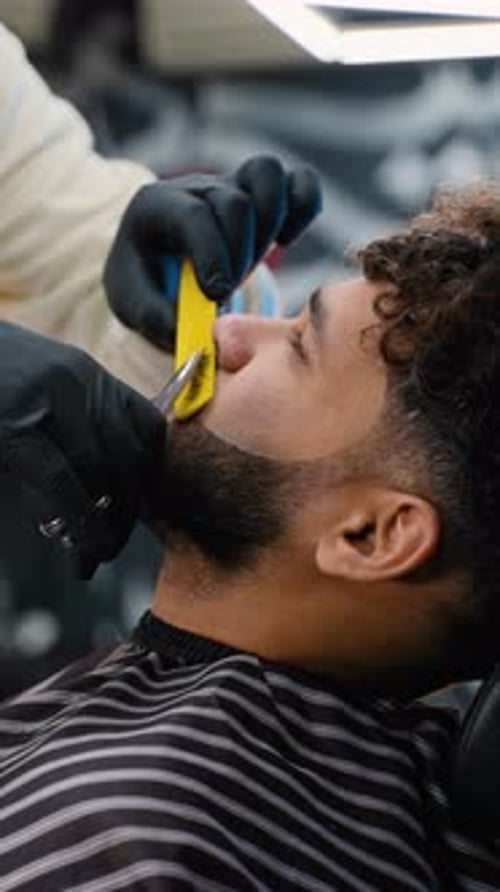 Professioneller Friseur, der den Bart eines Mannes mit einer Schere schneidet