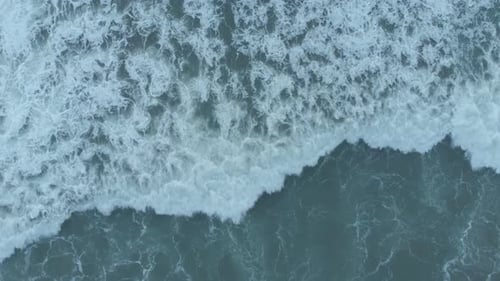 An overhead drone shot captures the textures of water as sea waves crush, foam, bubble, and swirl