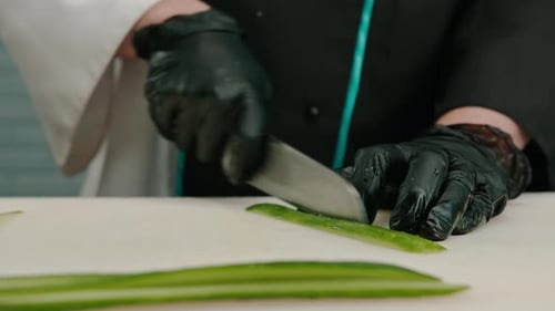 Close-up of a sushi maker in gloves cutting a cucumber with a professional kitchen knife